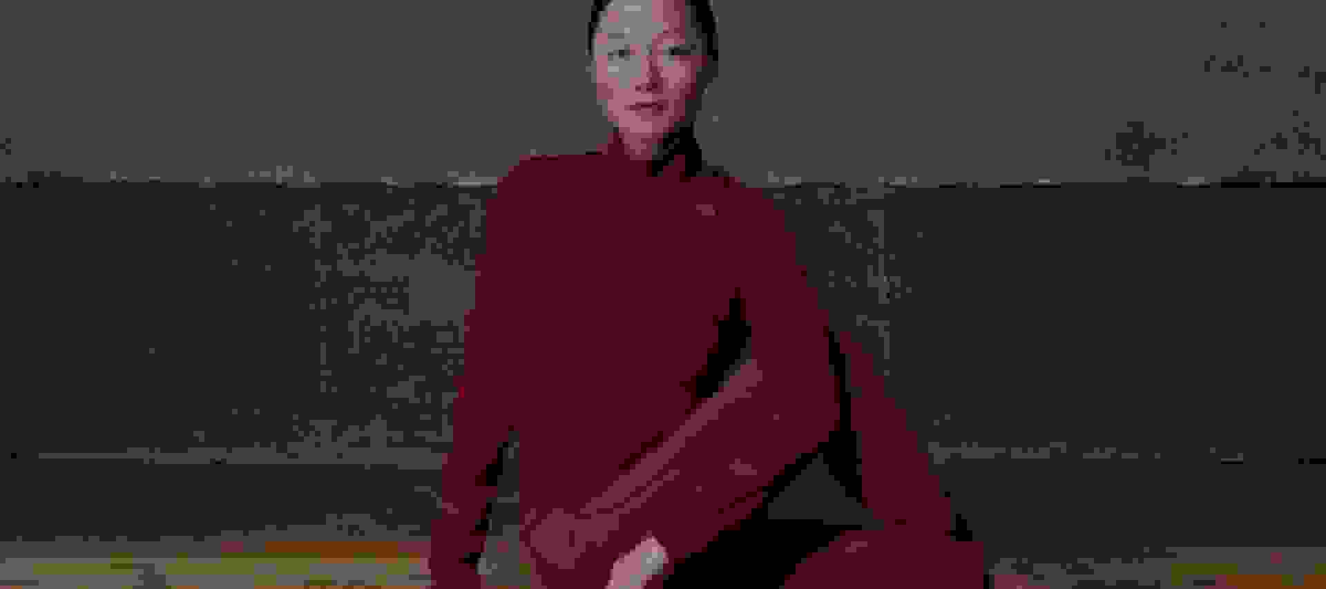 A person in a red leotard performing an acrobatic pose on a wooden floor against a dark background.