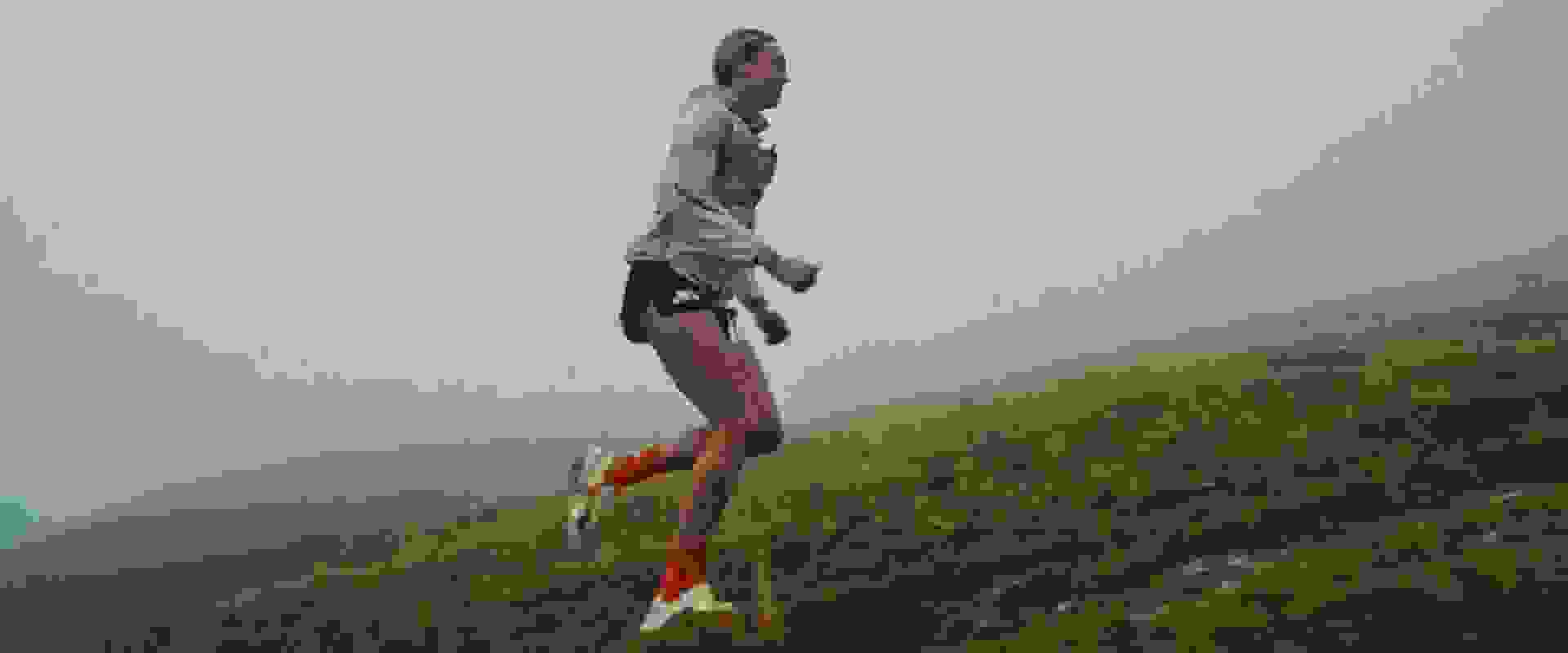 A winding mountain path leads through lush, verdant hills, with towering, cloud-shrouded peaks rising in the distance.