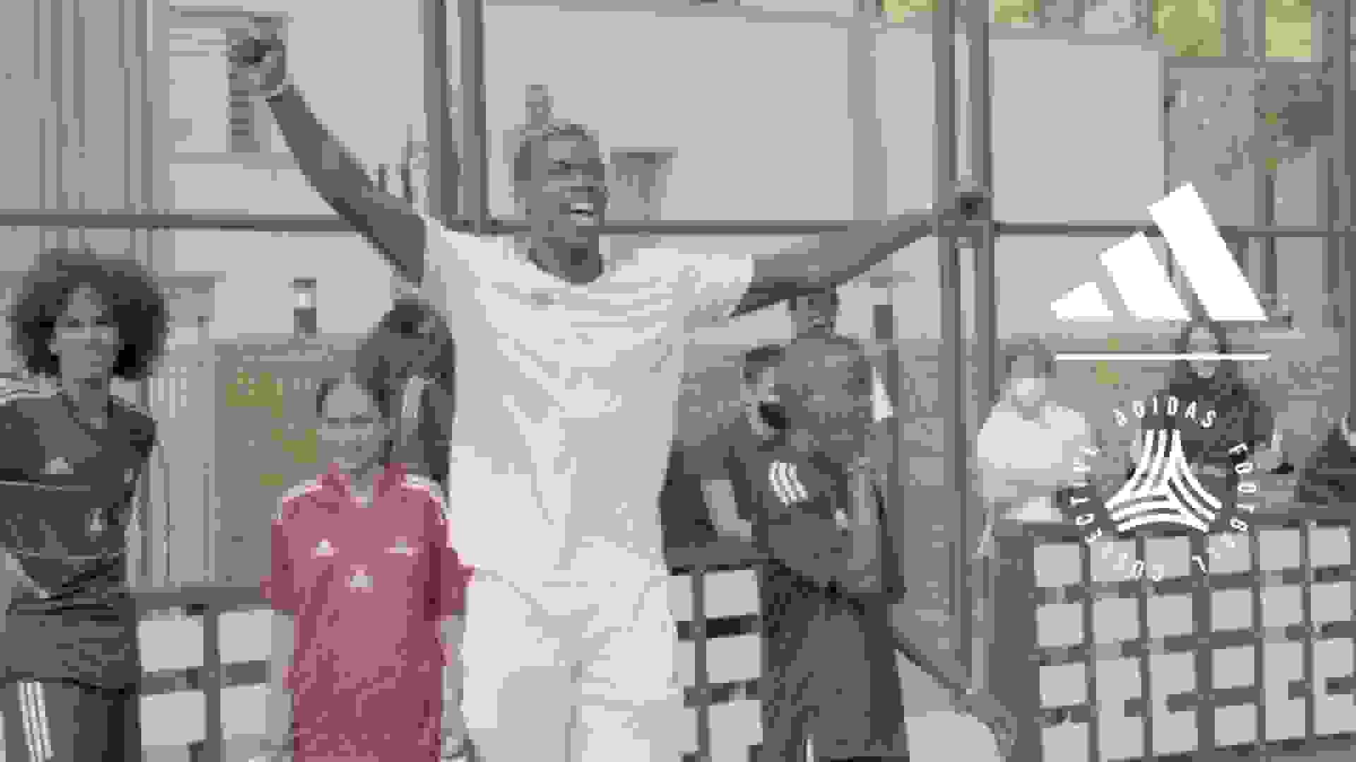 L'immagine mostra una persona che indossa una felpa con cappuccio e un cappellino neri, in piedi davanti a una lavagna con vari segni e simboli.