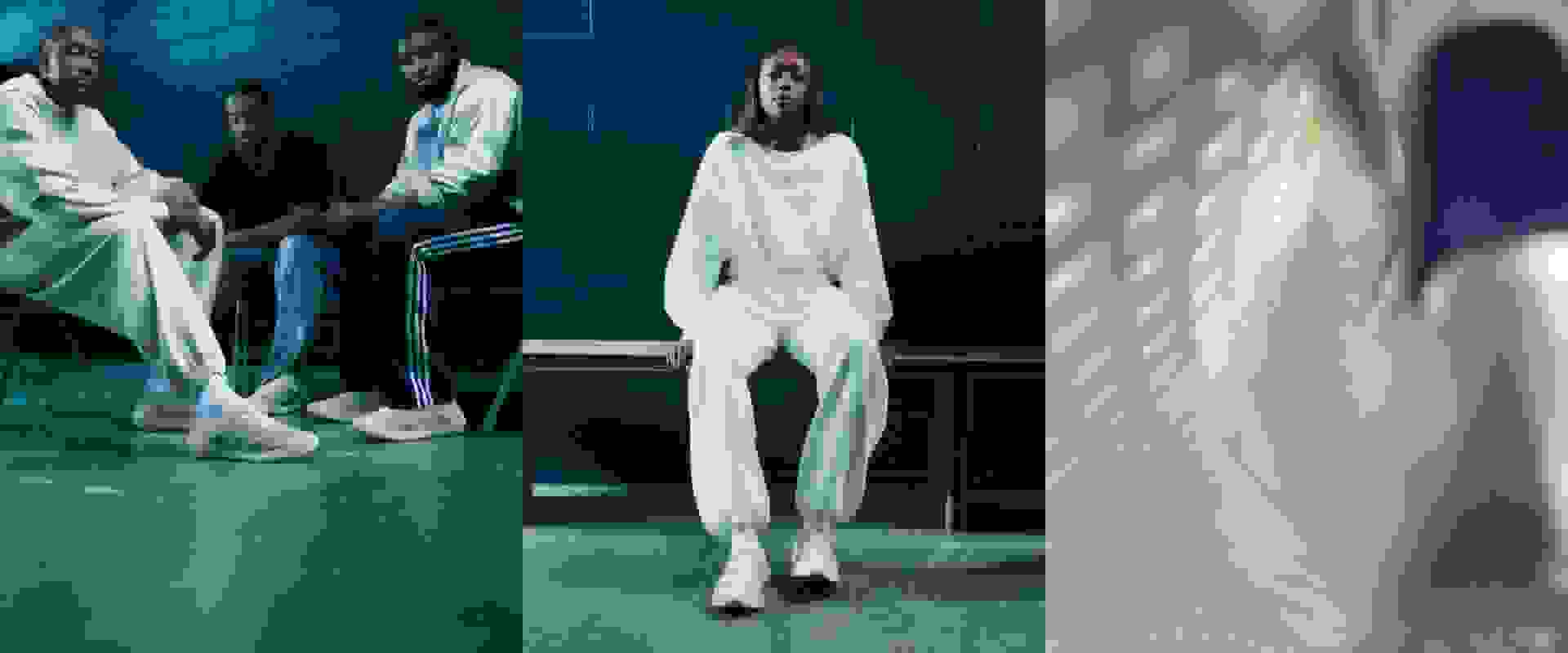 The image depicts a group of people in a dimly lit, blue-toned setting. In the foreground, a person wearing a white outfit stands on a raised platform, while others are seated around them.