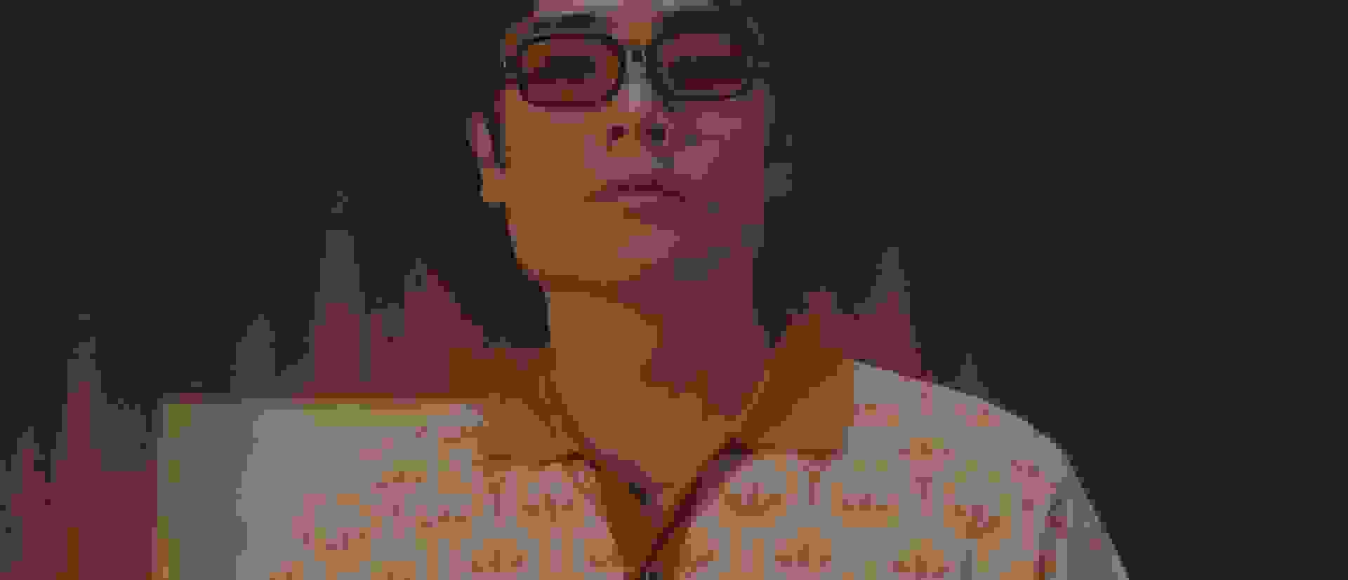 Člověk v šedém županu stojí v matně osvětlené místnosti, obklopený odpružením a dalším vybavením.