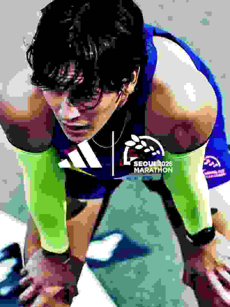 A female athlete in a blue and green athletic uniform is crouched on the ground, appearing to be in the midst of a running event or competition.