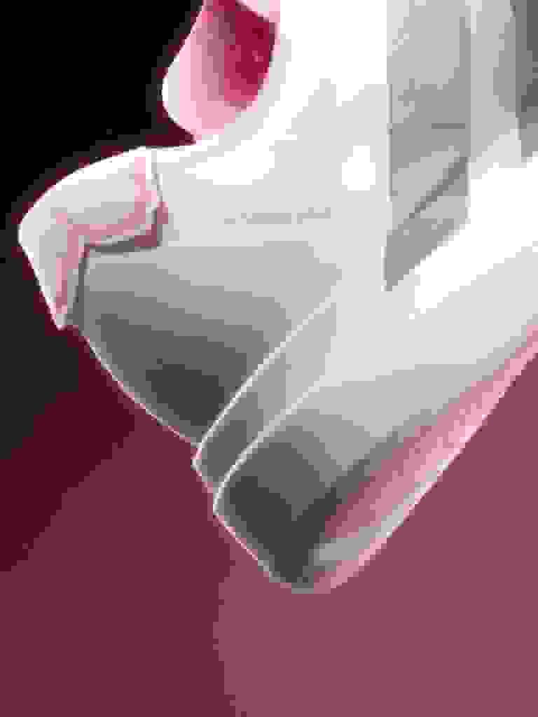 A white and pink athletic shoe with laces against a dark red background.