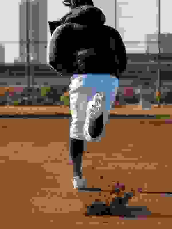 A pair of white athletic shoes with laces on a wooden surface, with a person's legs visible in the foreground.