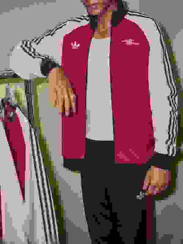 A young man wearing a white and red striped athletic top is seated in a wooden chair against a plain background.