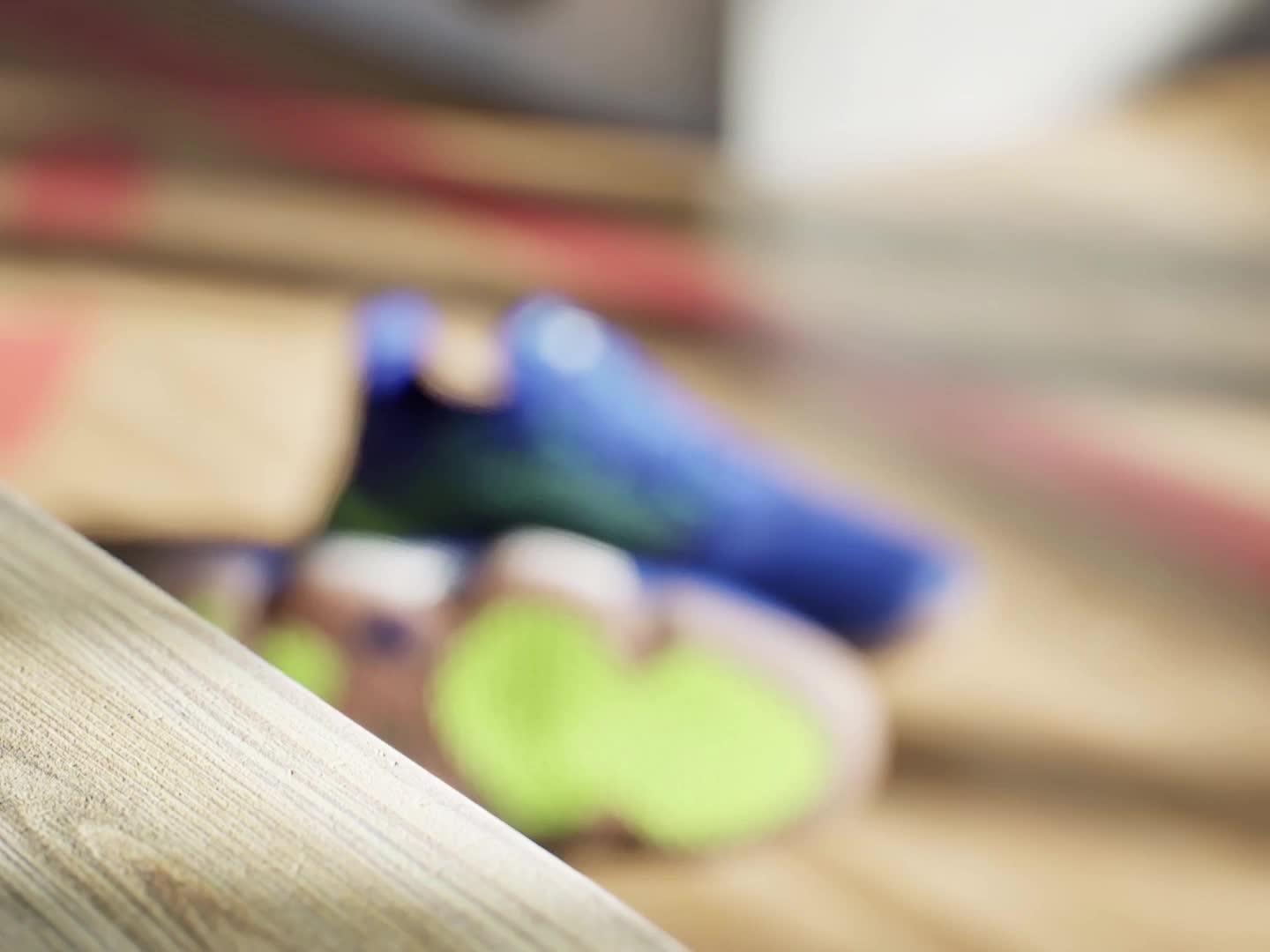 Zapatilla adidas azul y blanca sobre un suelo de madera con un fondo rojo y blanco a la vista.