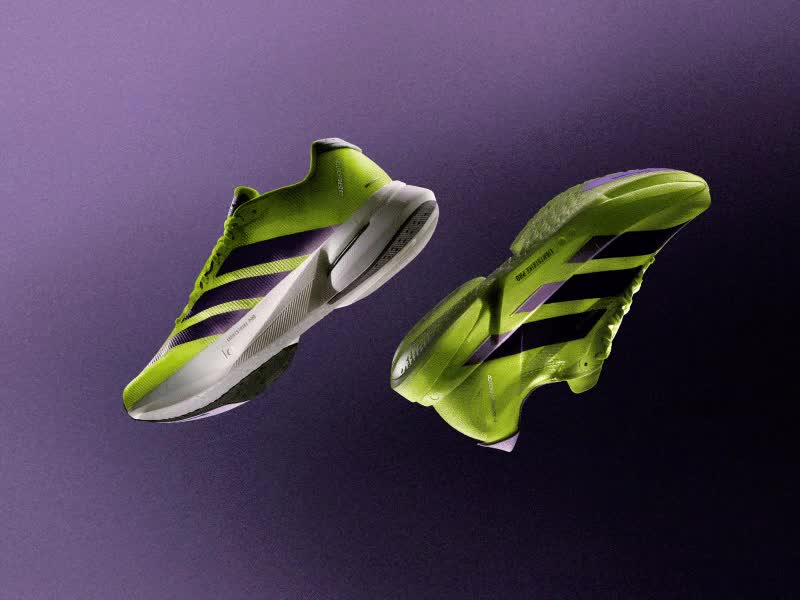 A male athlete in a yellow jersey and shorts is seen crossing the finish line with his arms raised in celebration, against a backdrop of a race event with banners and signage.