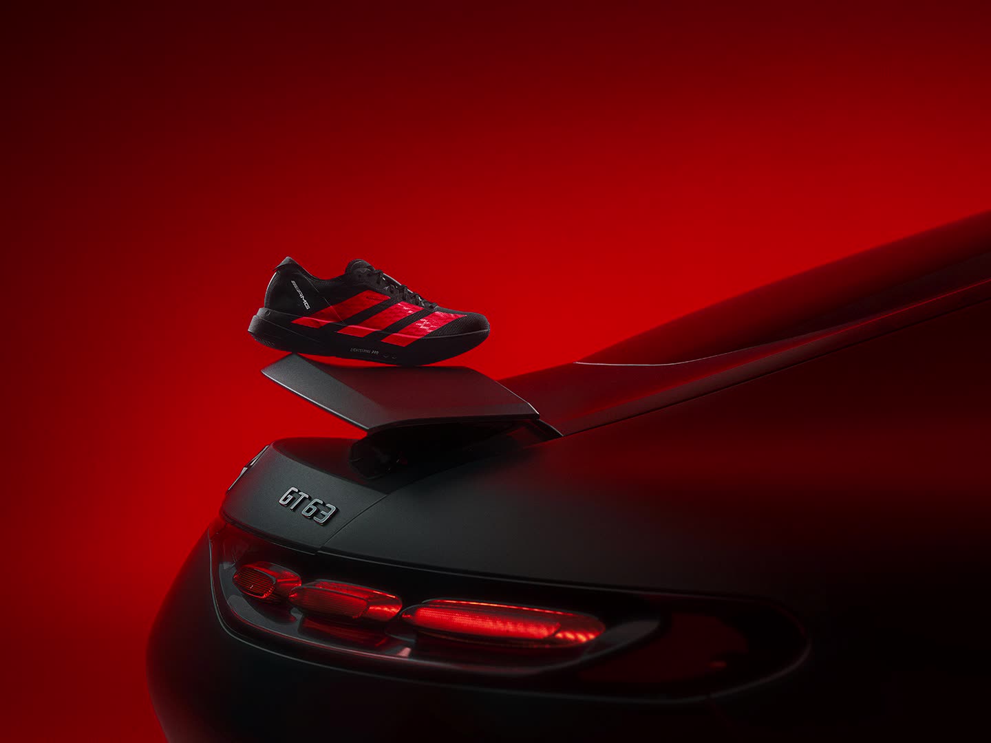 รองเท้ากีฬาสีดำและแดงที่มาพร้อมลายแถบสุดโดดเด่นตัดกับพื้นหลังสีแดงสด