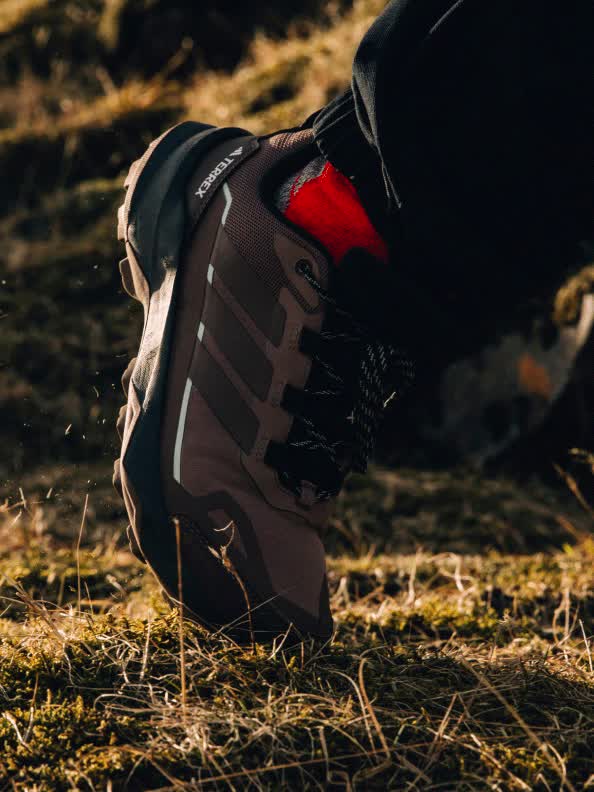 A pair of worn, dirty sneakers rests on a wooden surface, with a dark, shadowy background.