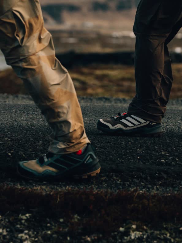 The image shows a pair of hiking boots standing on a rocky, uneven surface in an outdoor setting.