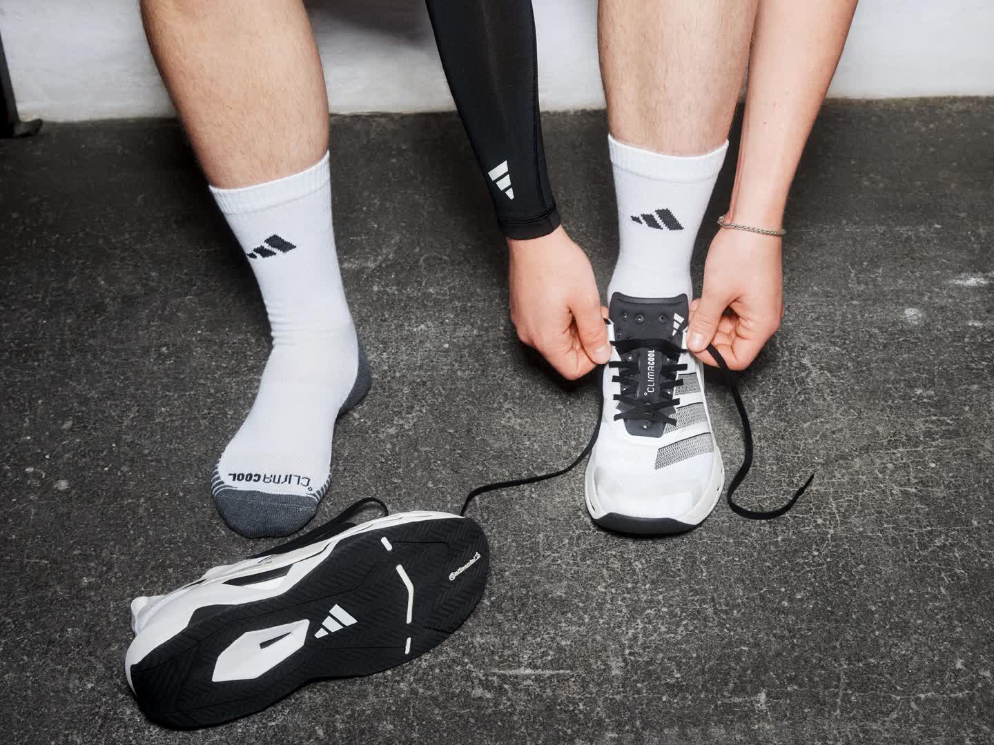 The image shows a person's lower body and legs performing an exercise on a ladder-like training device in a gym setting, with various fitness equipment visible in the background.
