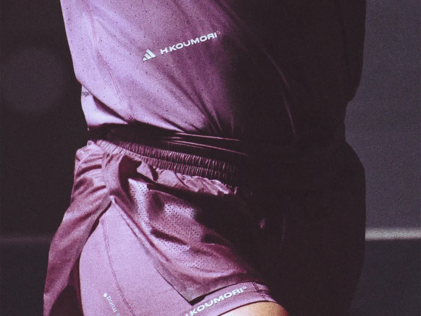 A person wearing a purple top and black pants is sitting on a dark surface, with a dimly lit background.