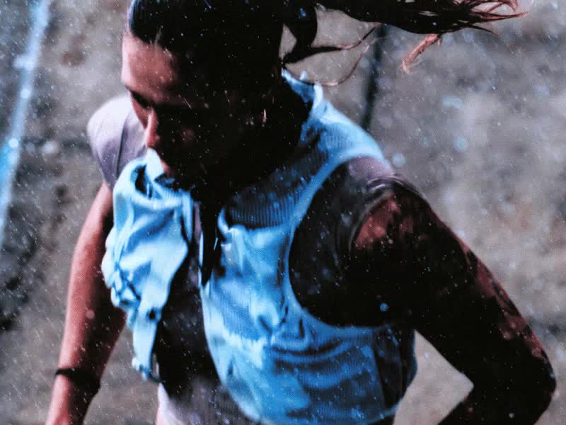 The image shows a pair of white and blue sneakers on a person's feet, standing in front of a dark, textured background.