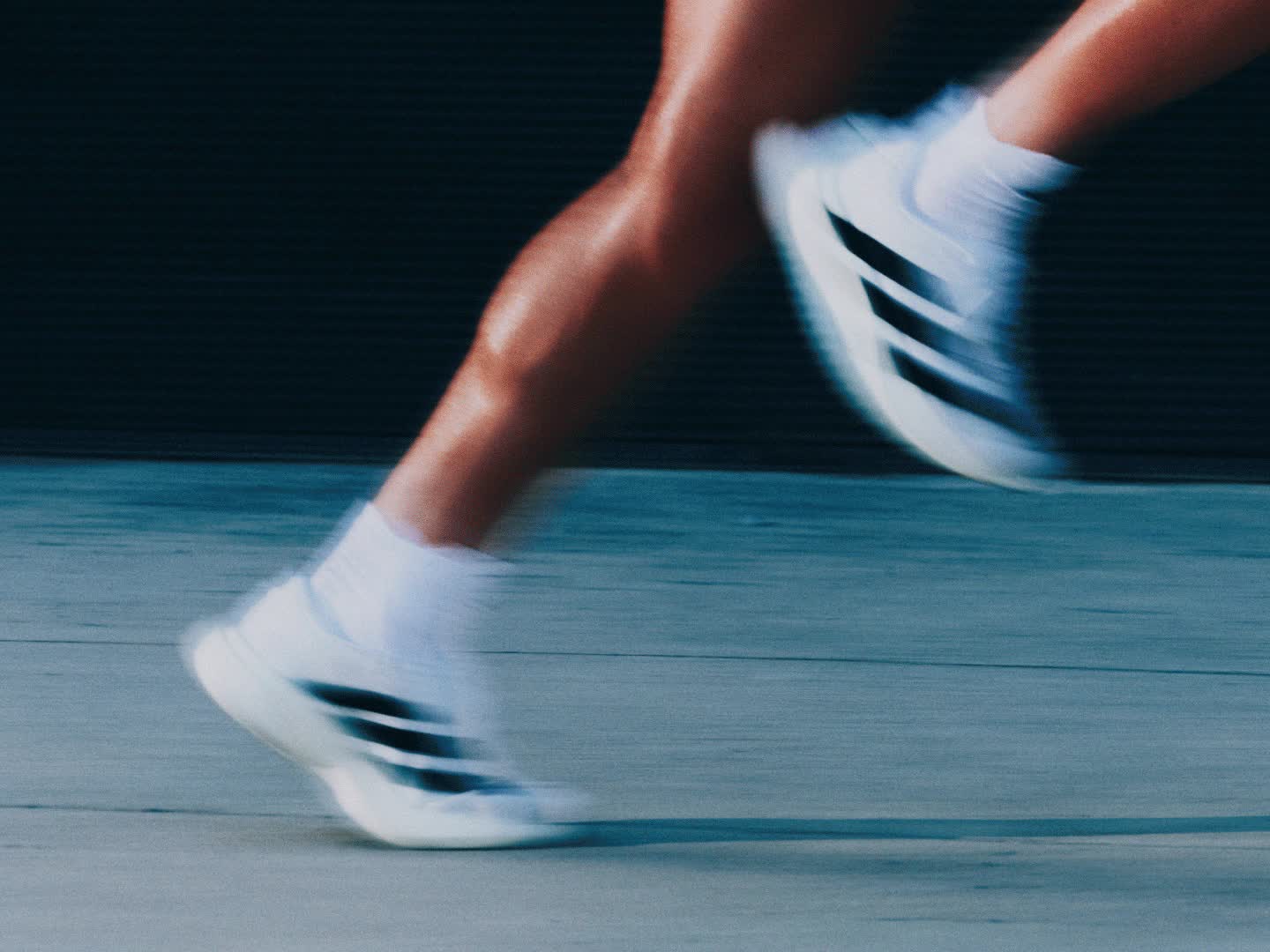 A person wearing a light-colored sleeveless shirt stands in a dimly lit setting, with a red background visible in the distance.