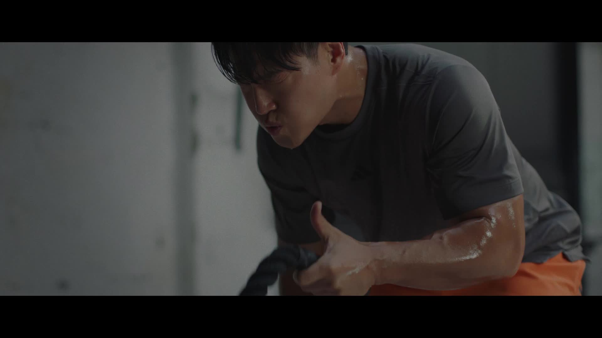 A person in athletic clothing sits on the floor in a dimly lit locker room, appearing pensive or distressed.