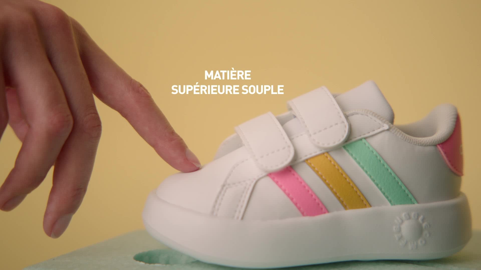 Une sneaker blanche ornée de bandes colorées sur un fond jaune uni.