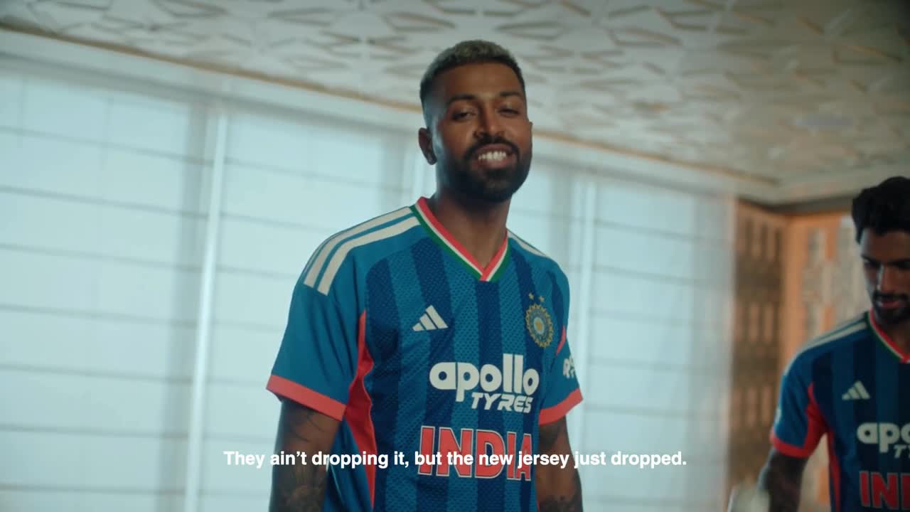Three individuals wearing blue and white sports jerseys are standing in what appears to be a locker room or changing area, with a patterned wall visible in the background.
