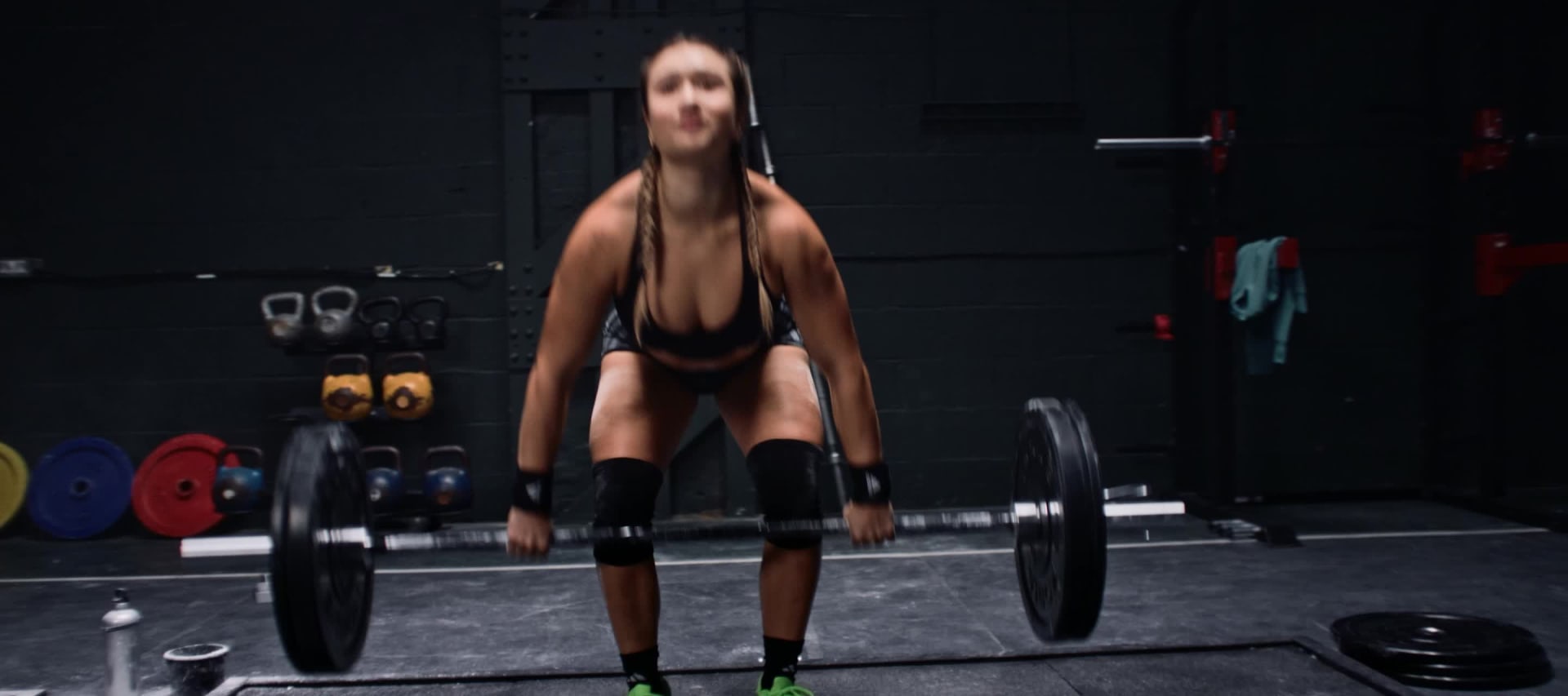 Woman lifting weights in black adidas workout clothes and green Dropset 3 shoes at the gym.