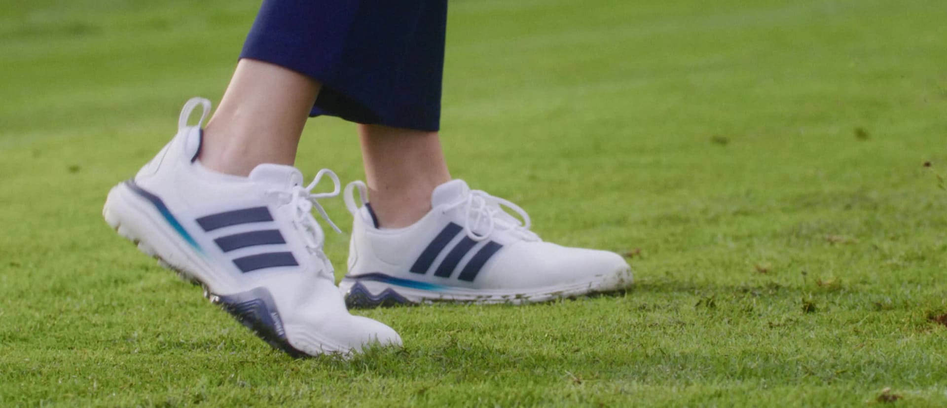 Bilden visar ett par vita och blå sportskor på en gräsbevuxen plan.