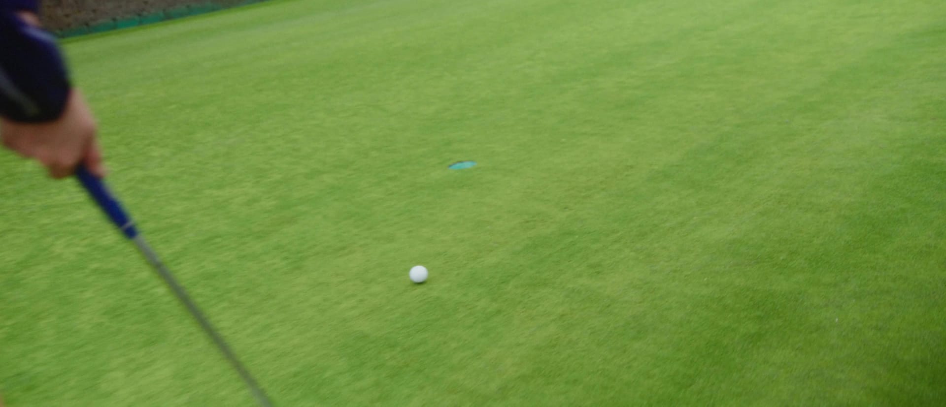 Na obrázku jsou nohy a nohy člověka v bílých teniskách stojících vedle černého vozidla na dlážděné silnici s trávou a stromy viditelnými v pozadí.