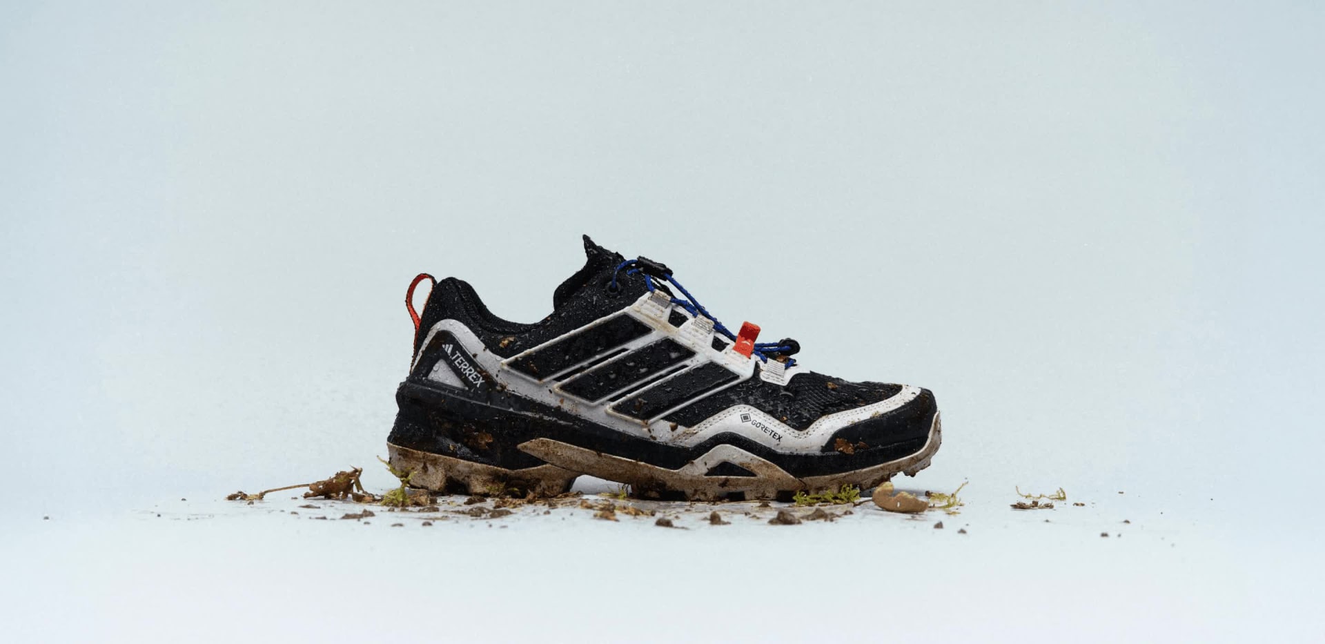 Looping images of adidas Skychaser hiking shoes against a grey backdrop, with dirt, leafs and other trail debris.