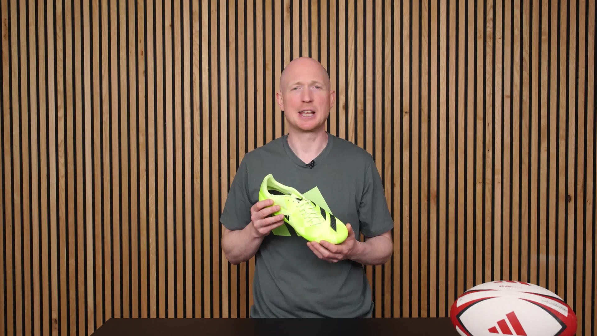 A middle-aged man wearing a gray t-shirt with the Adidas logo stands in front of a wooden slatted wall backdrop.