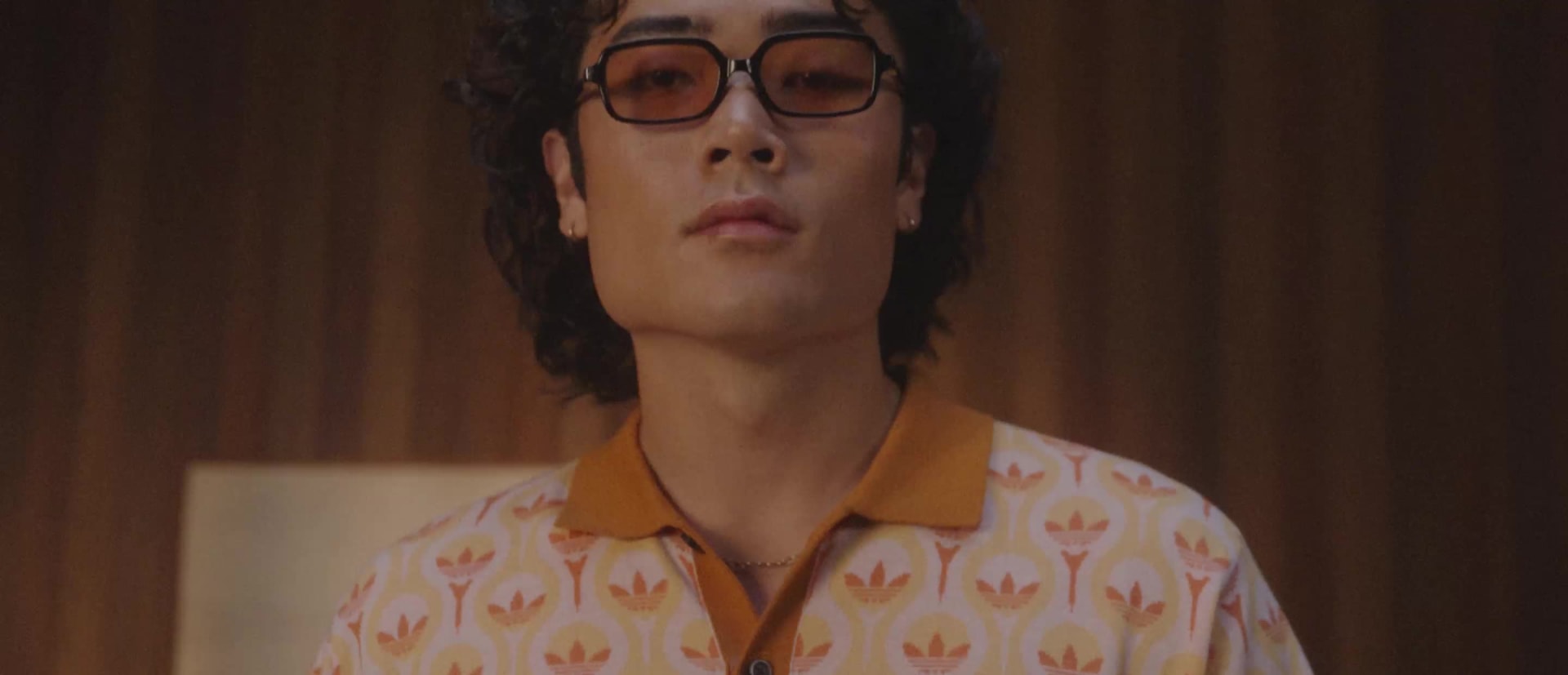 A person in a grey robe stands in a dimly lit room, surrounded by cushions and other furnishings.