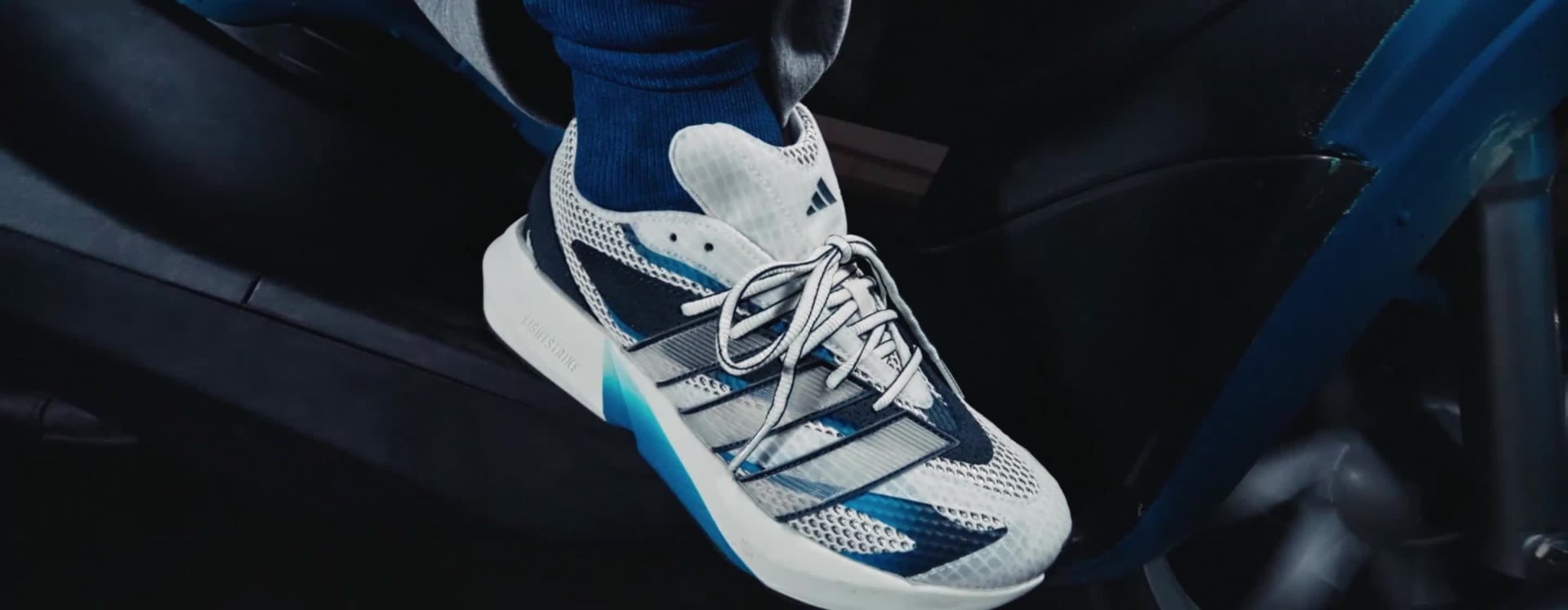 A person wearing a white robe stands in front of a building with a blue sky in the background.