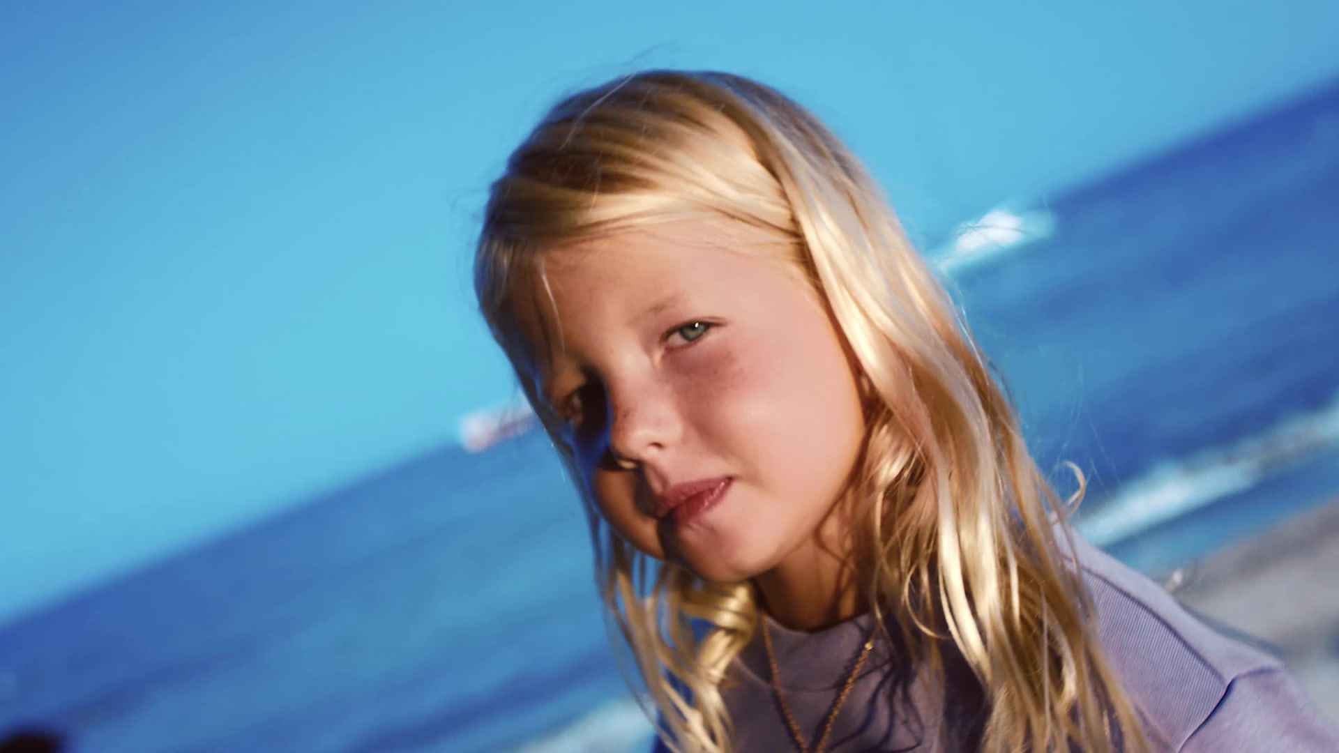 Two young children, a boy and a girl, stand on a rocky outcrop overlooking a vast, blue ocean under a clear sky.