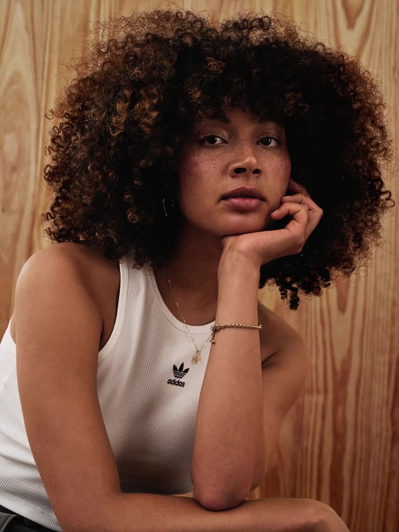 Model reclines on chair wearing off-white jacket and pants and beige adidas sneakers