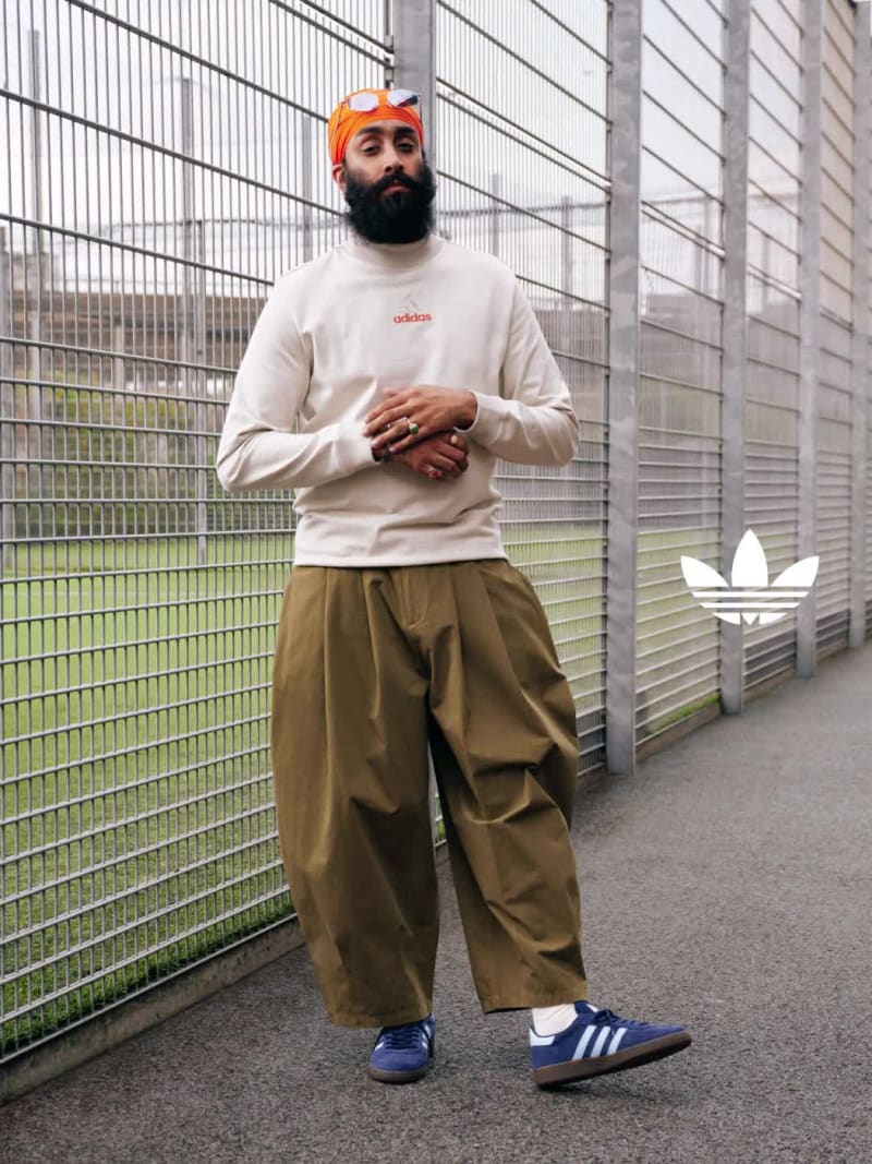 A man and a woman in adidas apparel model white and black adidas Handball Spezial sneakers outside a tennis court.