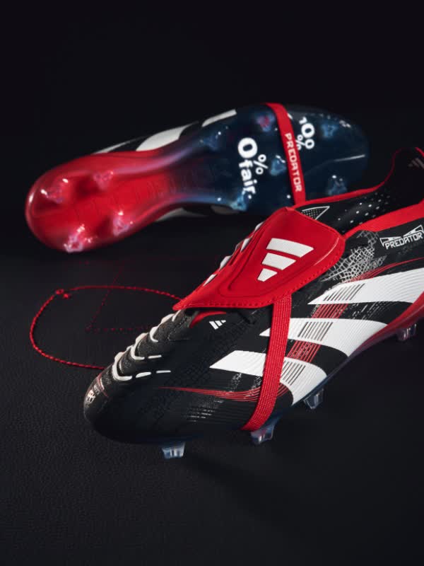 The image shows a pair of red and black soccer cleats with the Adidas logo prominently displayed. The cleats are positioned on a dark background, creating a dramatic and moody atmosphere.