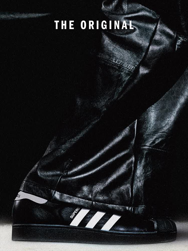 Person in a black Adidas Firebird jacket stands with arms outstretched in a crowded space; Superstar and Adidas logo are visible against a dark background.