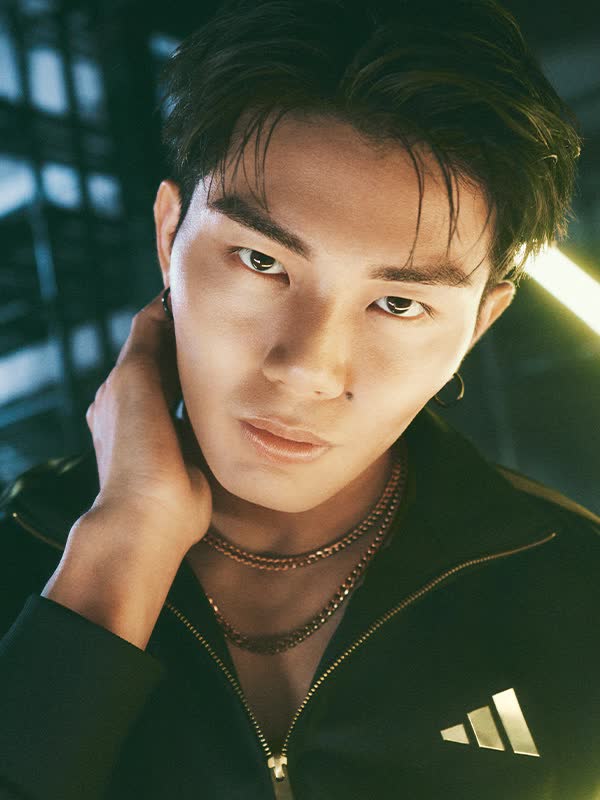 A young man wearing a black jacket stands in a dimly lit room, surrounded by glowing neon lights that create an atmospheric and dramatic setting.