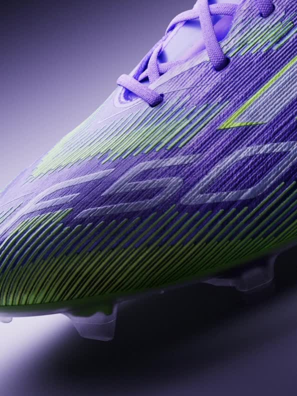 A sleek, purple-colored sports shoe is prominently displayed against a dark background, with a beam of light illuminating its contours.